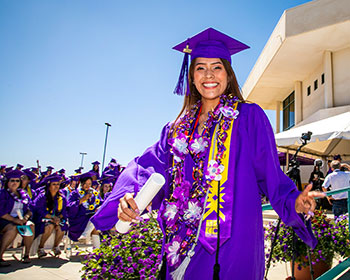 Graduate walking down platform holding diploma with flowers in background