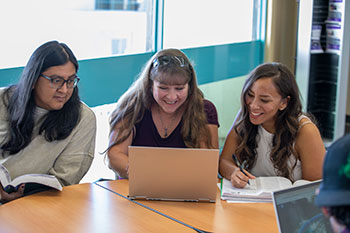 Three students smiling at open computer on table.