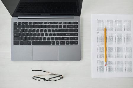  Top view of a table with a laptop, glasses, pencil, and exam sheet on it